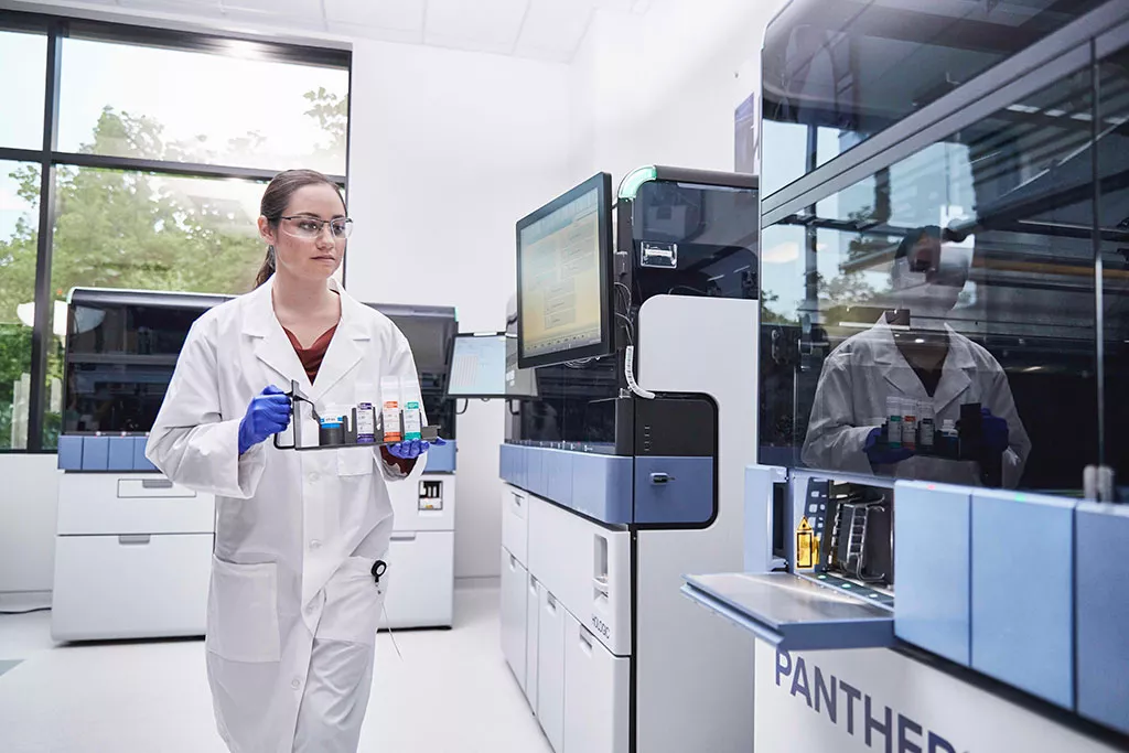 Laboratorietekniker som bär en bricka med prover som ska sättas in i Panther-systemet